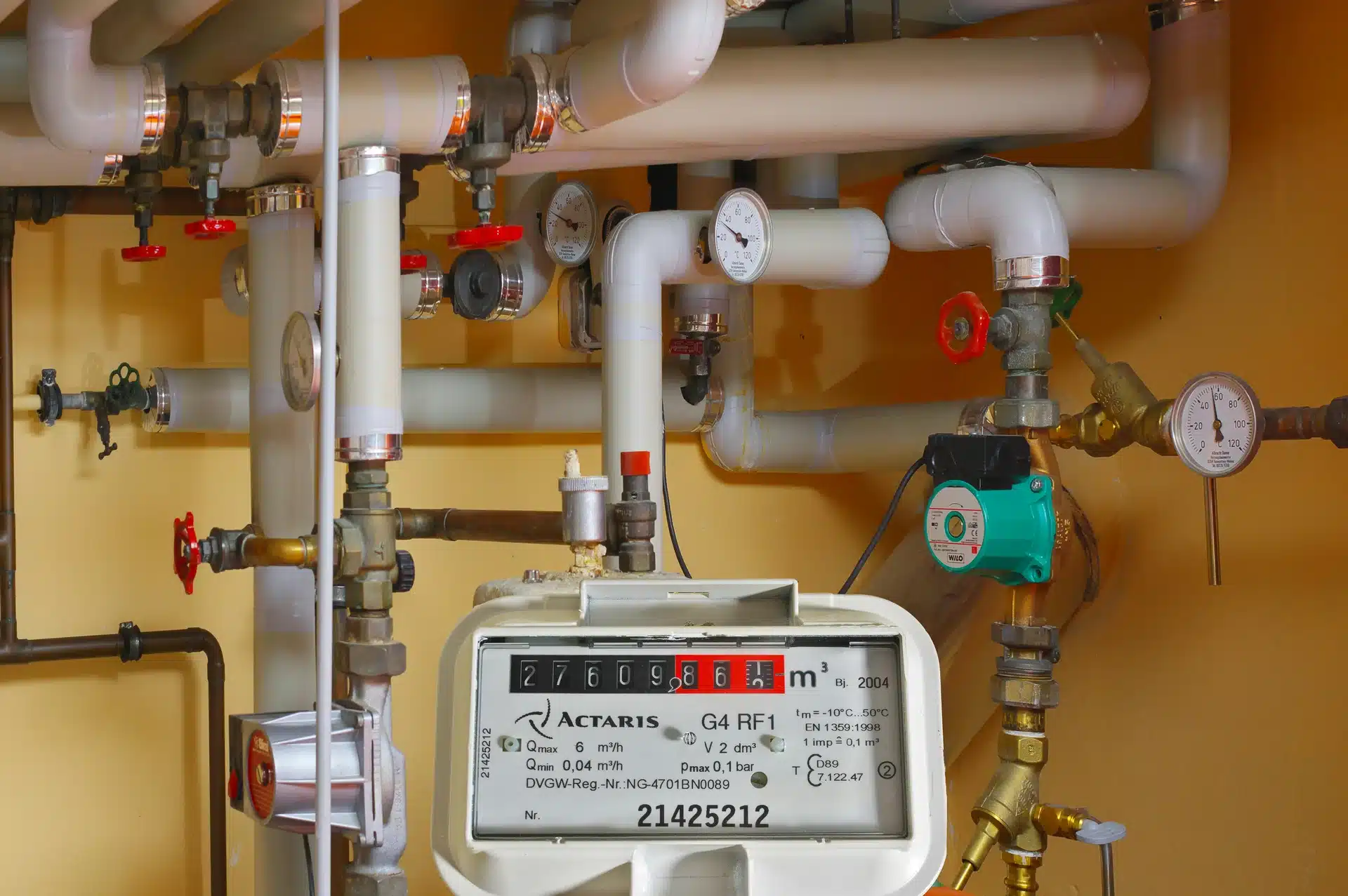 A professional plant room installation featuring an Actaris gas meter, insulated heating pipes, pressure gauges, and a Wilo circulating pump.